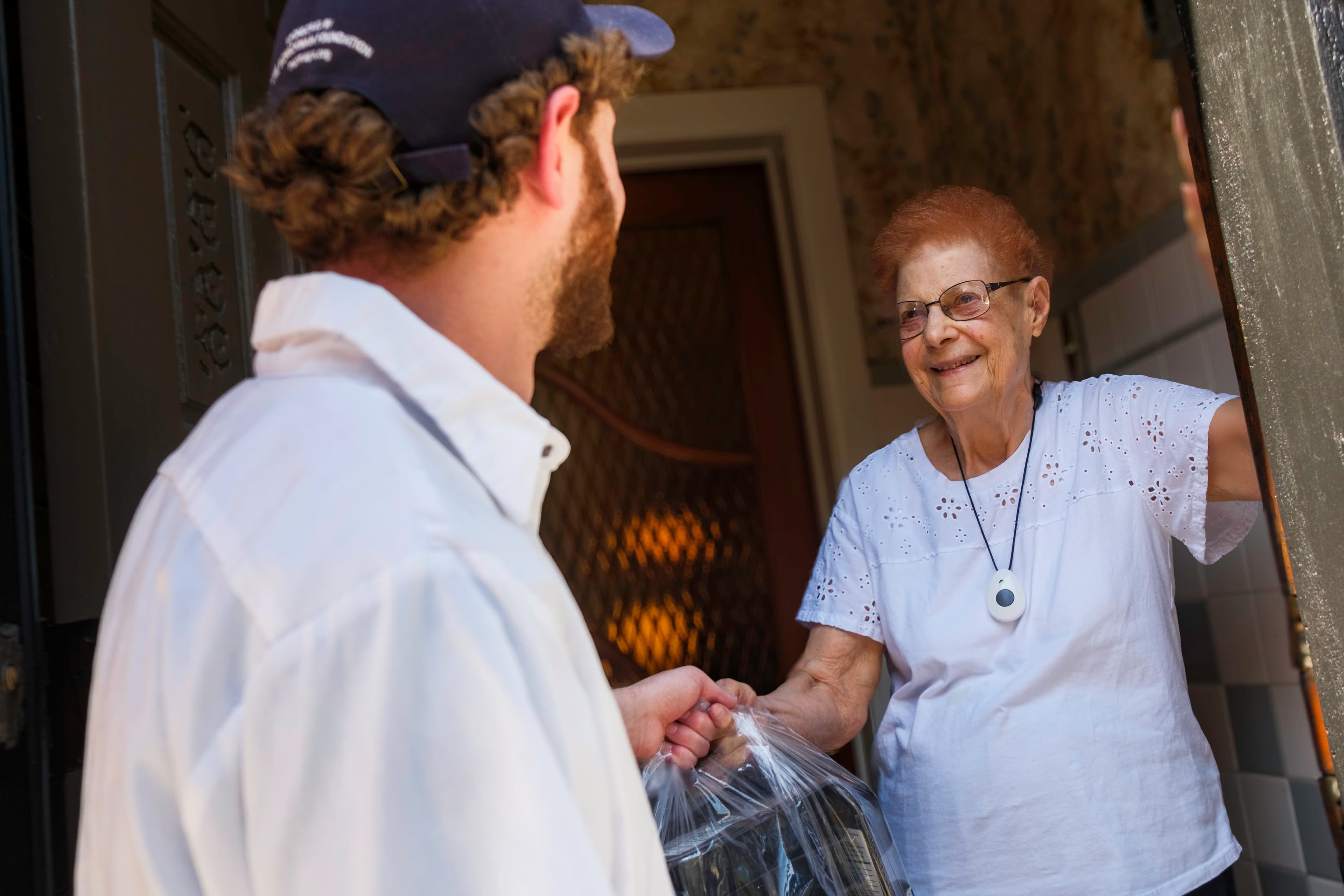 MANNA driver hands a bag of dinners to a smiling client standing in their doorway